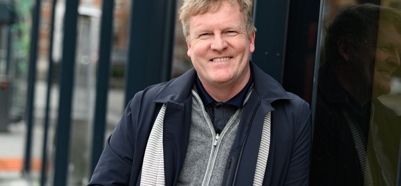 Øystein Strand smiler til kamera, står ved en bygning ute