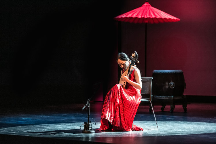 Kvinne spiller kinesisk instrument på scenen i rød kjole