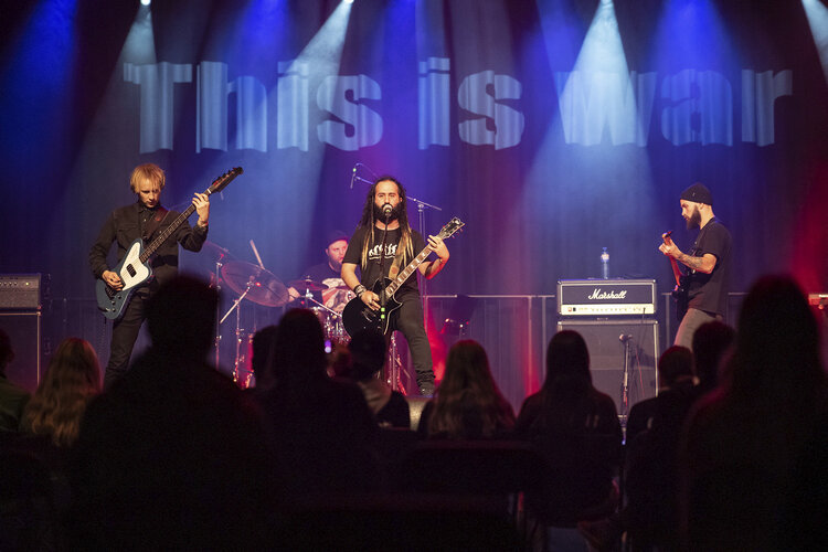 Confess opptrer på scena. "This is war" står det på veggen bak dem.