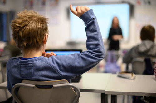 gutt som rekker opp hånden i ett klasserom