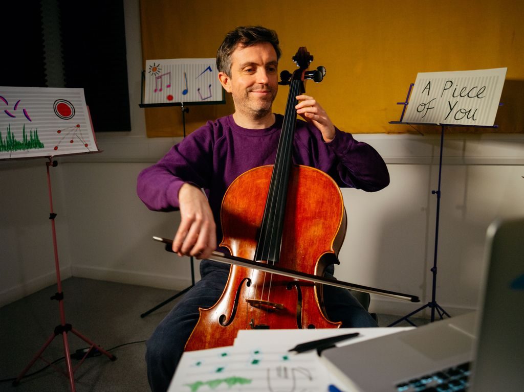 En musiker spiller cello for en publikummer som følger med via en datamaskin