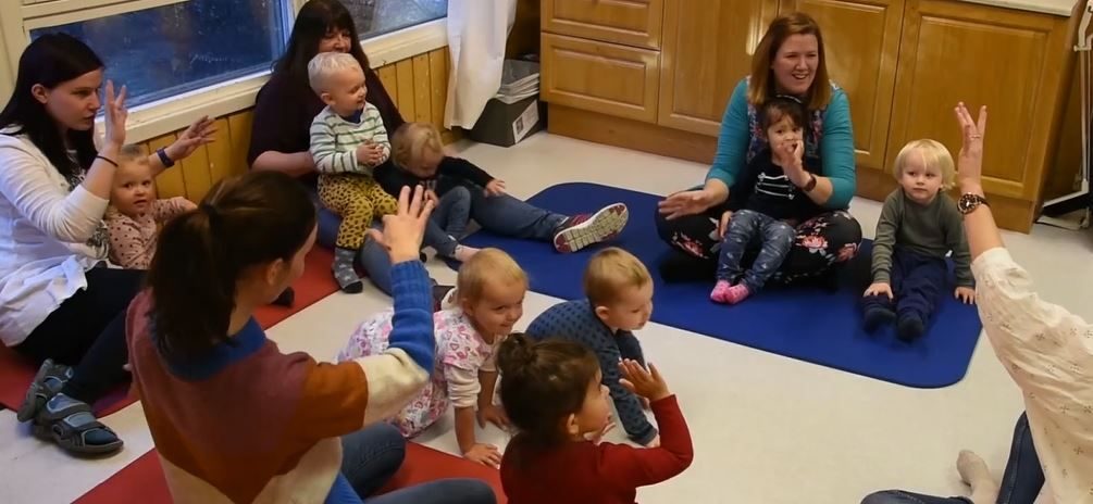 Barn og voksne sitter sammen. Følger håndbevegelser til utøver.