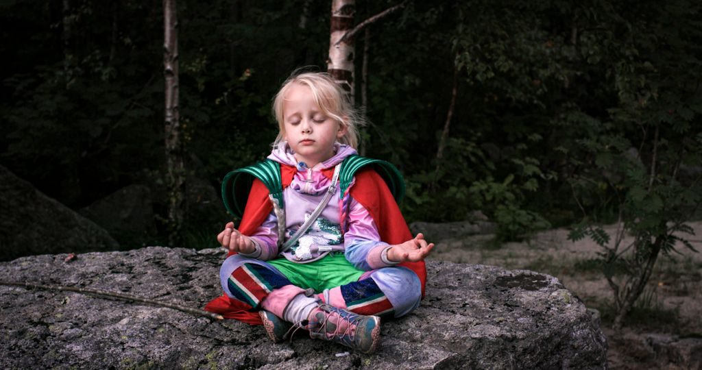 En liten jente sitter i rød kappe på en stein med øynene lukket