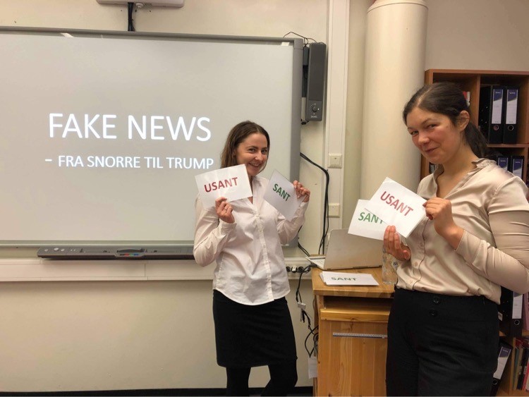 To kvinner holder opp lapper foran en skjerm der det står "Fake News"