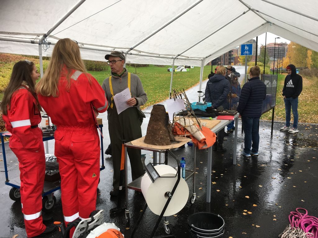 To jenter i røde heldrakter ler og prater med en lærer