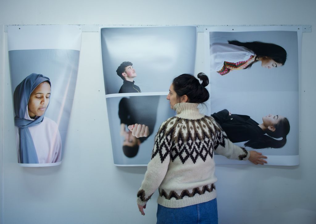 En kvinne står foran tre store portretter som er hengt opp på veggen