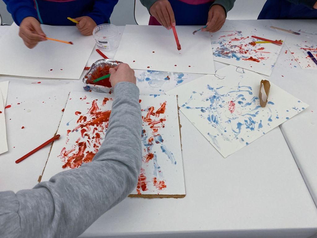 Hender som maler i rødt og blått på papir som ligger strødd utover et bord