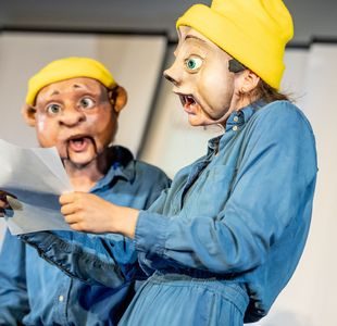 To skuespillere i komiske masker leser fra et ark