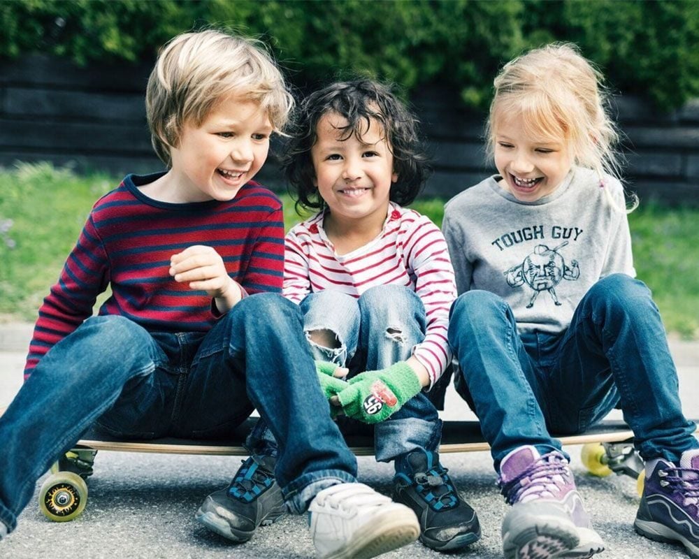 Tre barn sitter på et skateboard