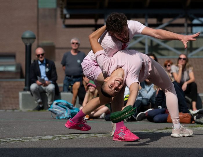To dansere holder og danser rundt hverandre på en skolegård mens publikum ser på i bakgrunnen