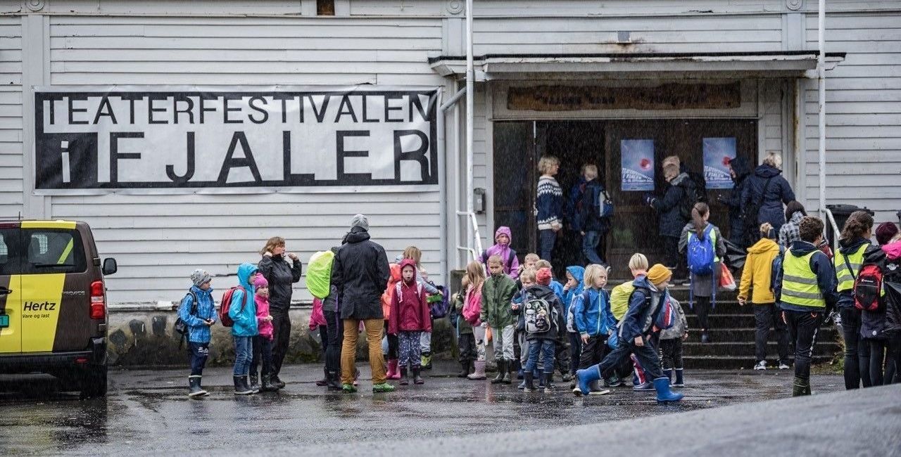 barn står u tenfor et bygg hvor det står "Teaterfestivalen i Fjaler" på et banner