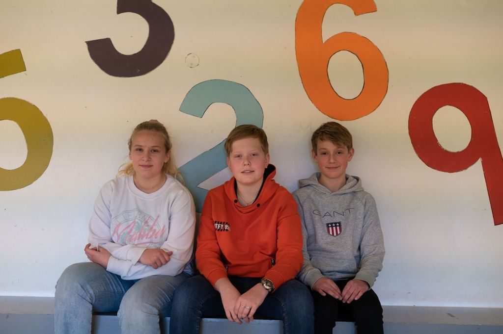 Tre ungdommer sitter på rad og rekke foran en vegg med tall