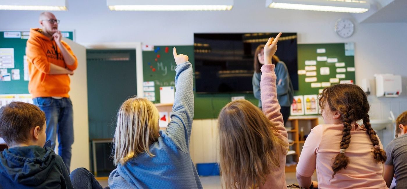 Elever rekker opp hånda i klasserommet.