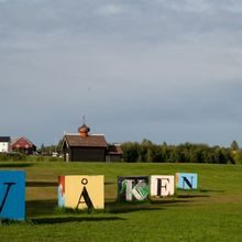Treblokker med bokstaver som utgjør ordet "våken" står på en gressplen foran en gård