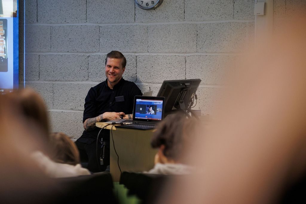 Kontaktlærer Øystein Gjerde Nilsen sitter foran noen PC-skjermer, ser ut på klassen og smiler.
