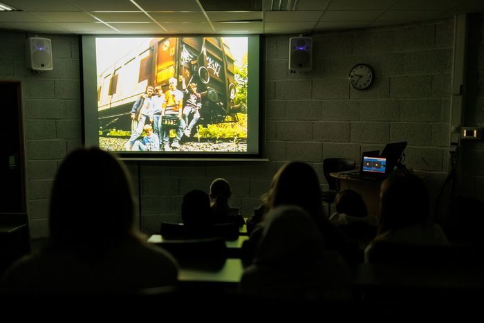Stillbilde fra filmen "Togrøvere", med en ungdomsgjeng foran en togvogn, vises på skjerm i auditorium.