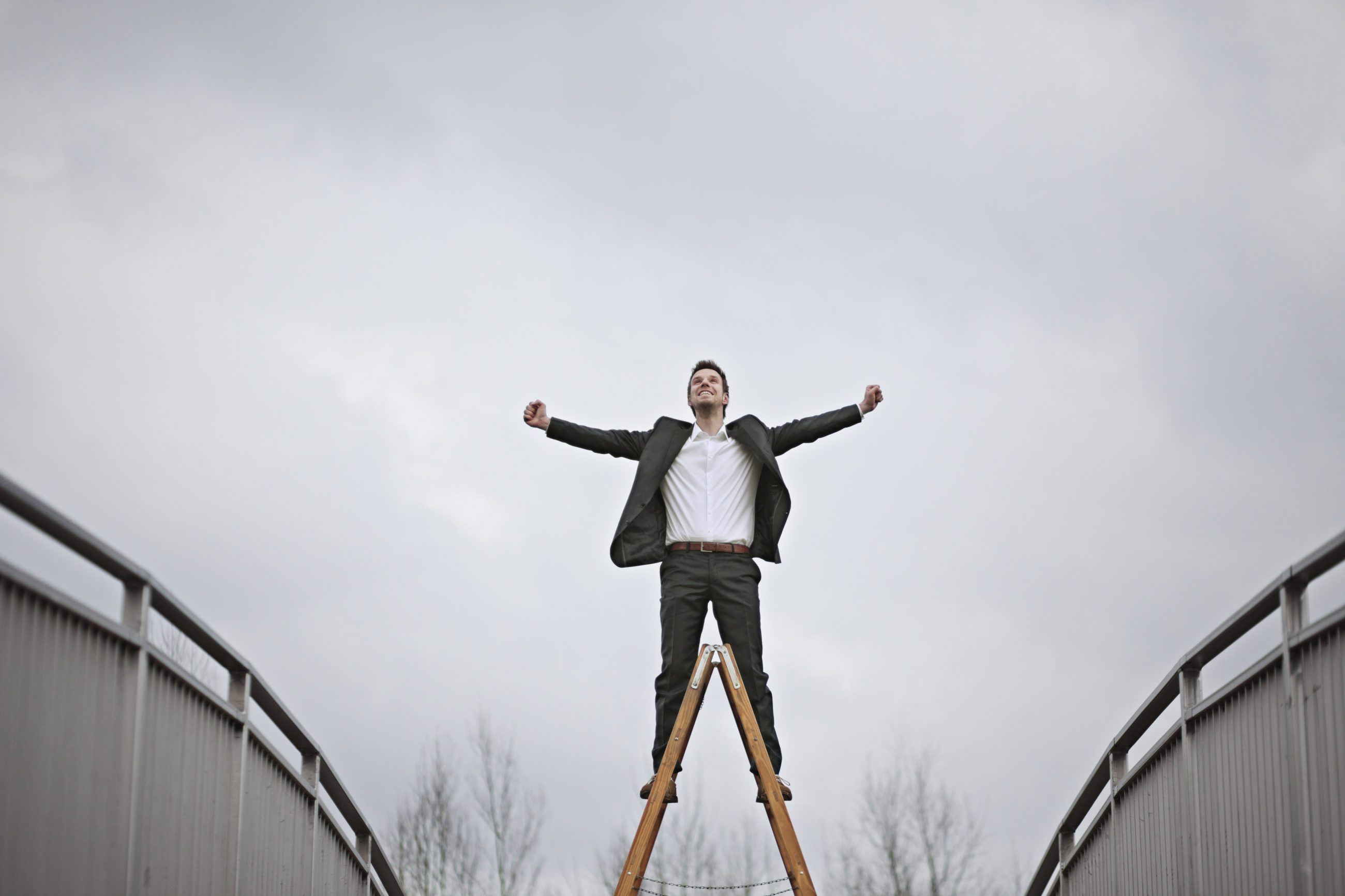 Mann står på toppen av en vinklet stige med armene opp.