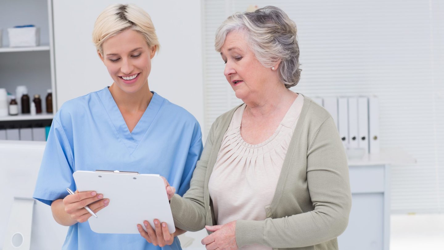 Kvinnelig sykepleier kommuniserer med eldre, kvinnelig pasient.