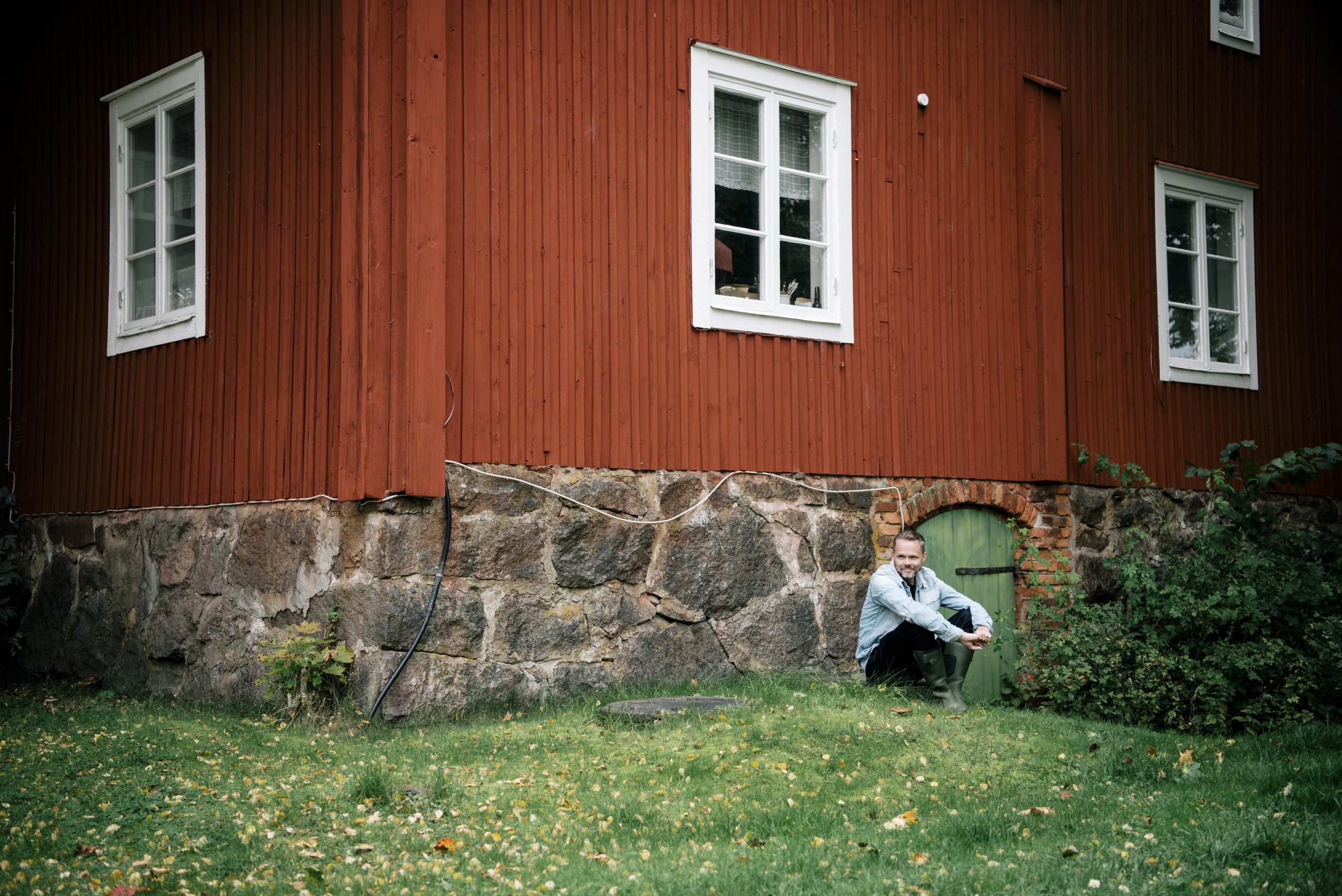 Mikael genberg sitter på huk foran en rød stugu.