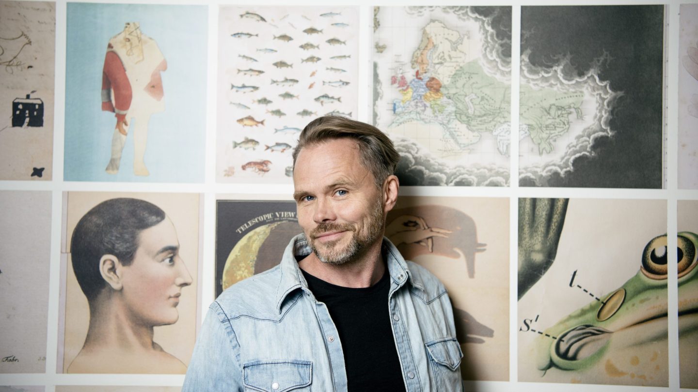Mikael Genberg står foran en vegg med ulike kunstbilder.