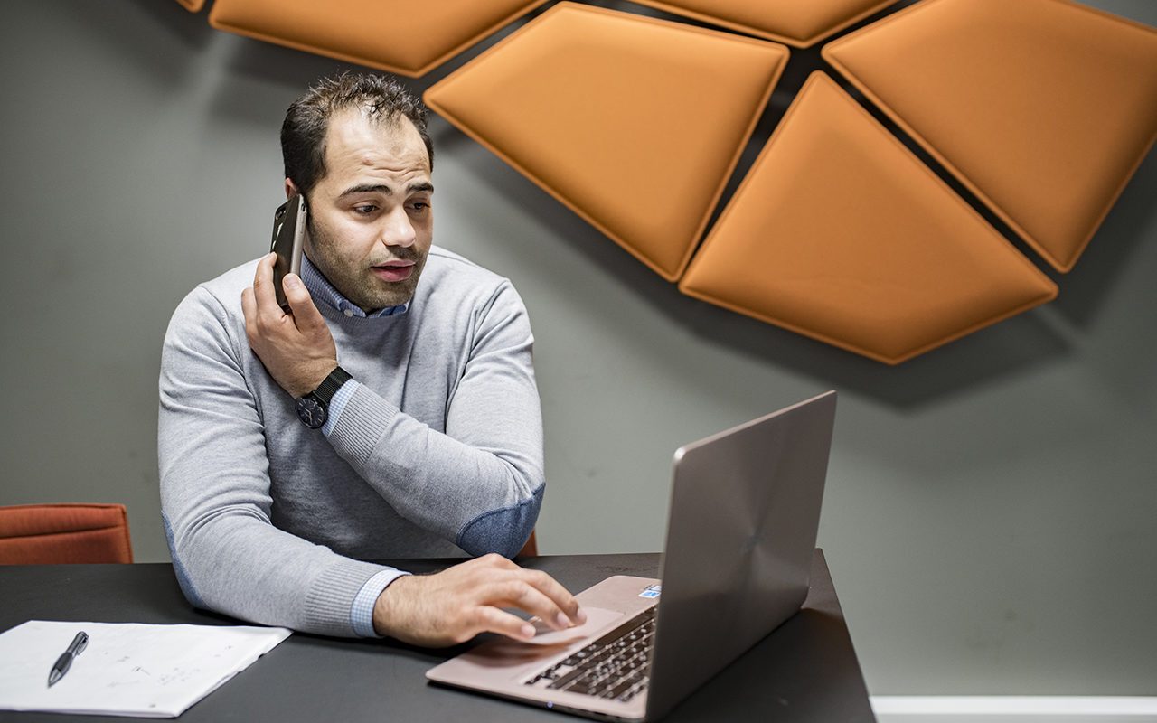 Integrering og inkludering: Mann sitter og jobber ved laptop, med en telefon mot øret.