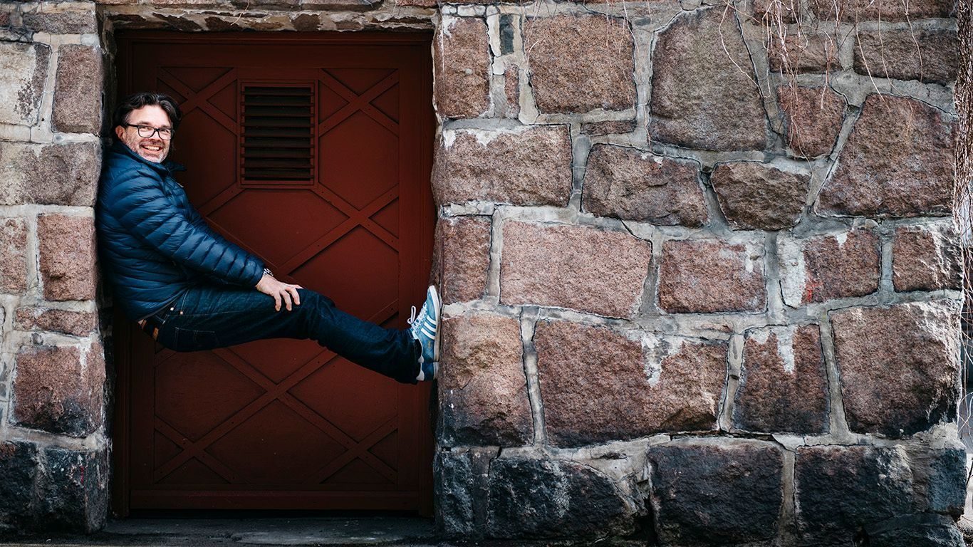 Nysgjerrighet: Smilende mann sitter i spenn i en gammel dørkarm.