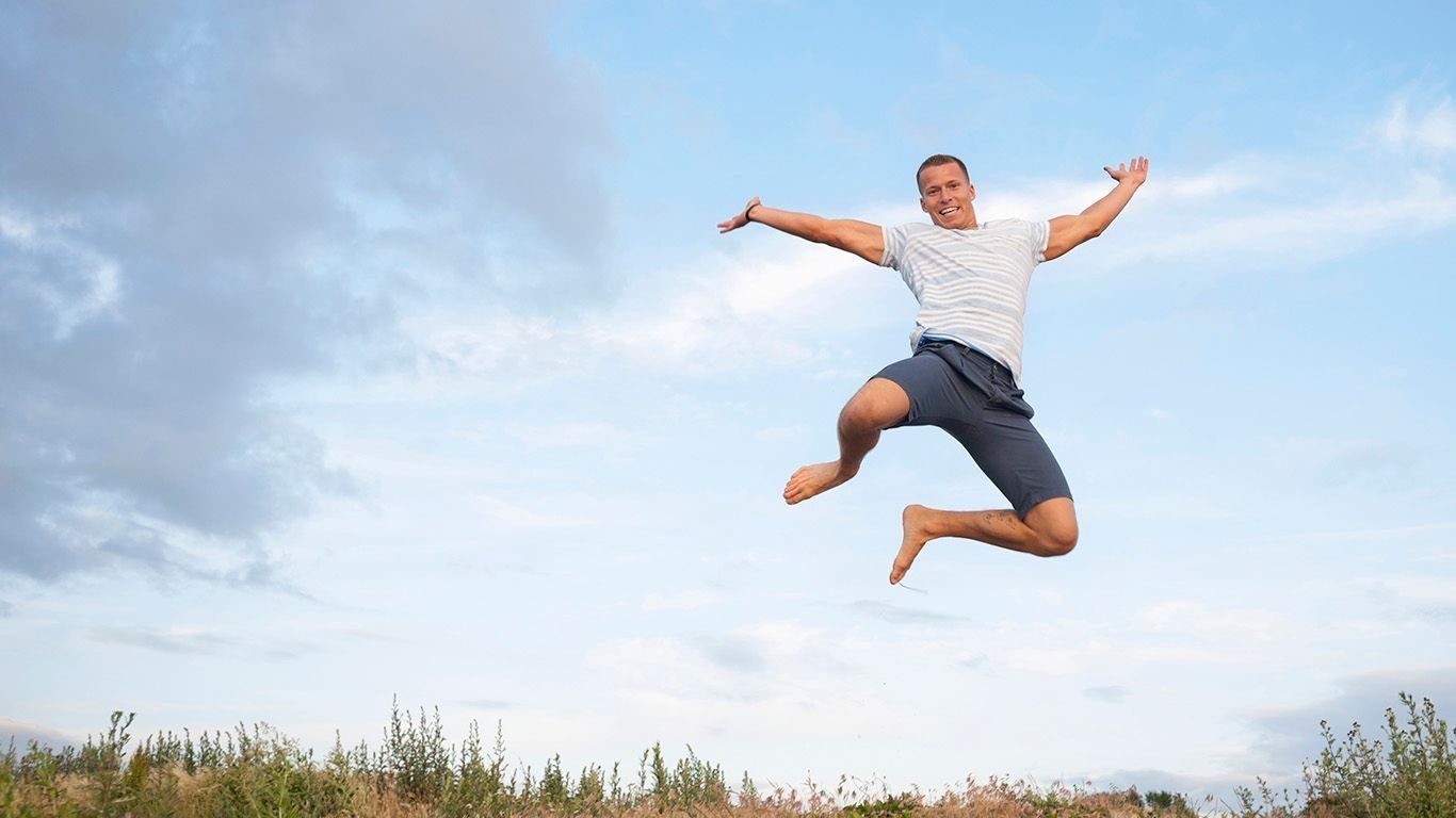 Endring: Glad mann hopper høyt ved en strand.