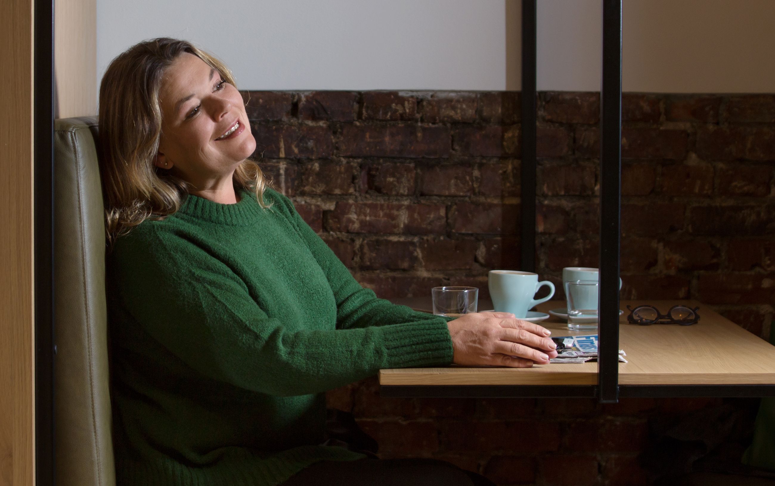Verdier: Kvinne i grønn genser sitter i en kafébås og smiler.