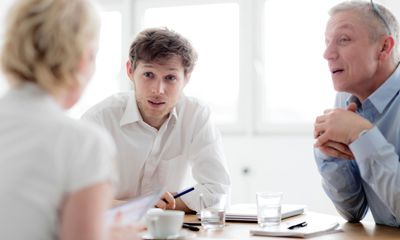 Personligheter: En kvinne og to menn snakker sammen rundt et bord. Kvinnen sitter med ryggen til.