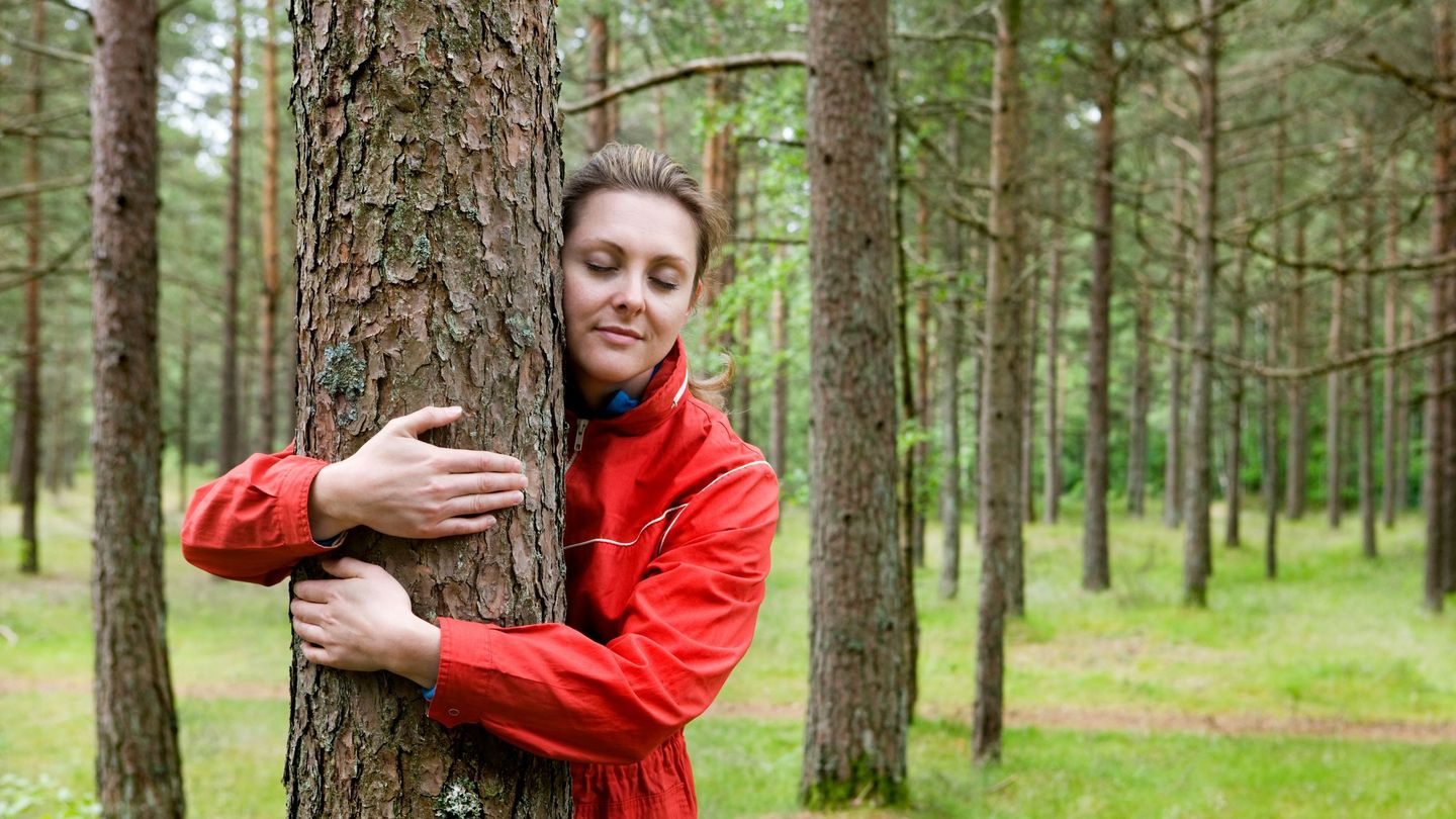 Balanse: Kvinne med rød ytterjakke omfavner et tre i skogen.