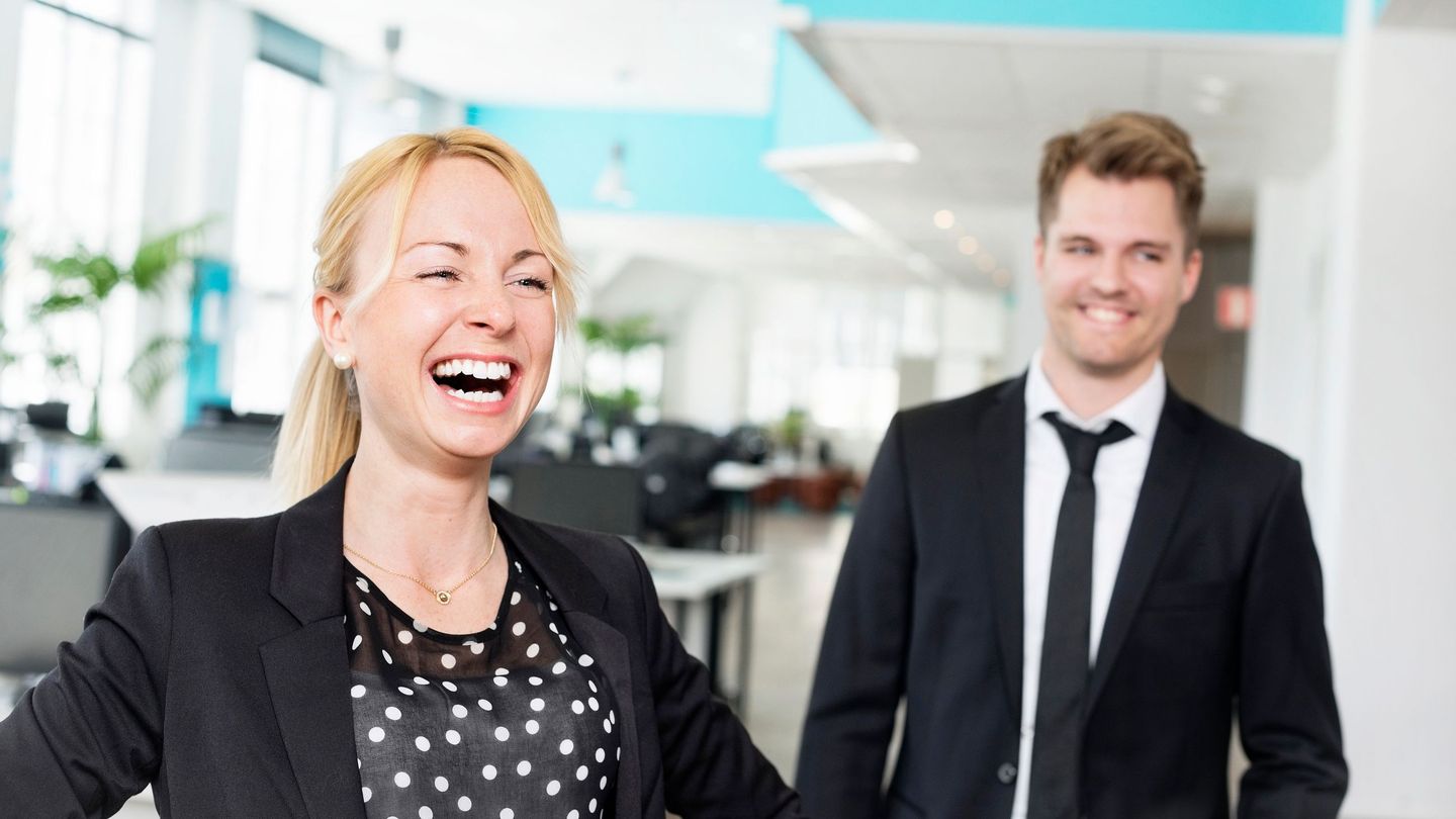 Motivasjon: En kvinne ler og en mann smiler i et kontorlandskap.