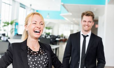 Motivasjon: En kvinne ler og en mann smiler i et kontorlandskap.