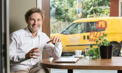 Kulturer: Blid mann sitter ved et bord, og utenfor kjører en gul pizzabil forbi.