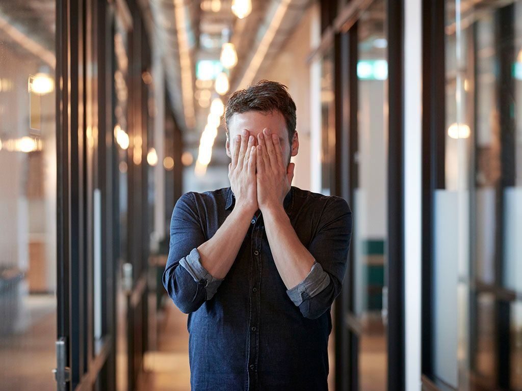 UUtbrent: Ung mann står i et kontormiljø og holder hendene for ansiktet.