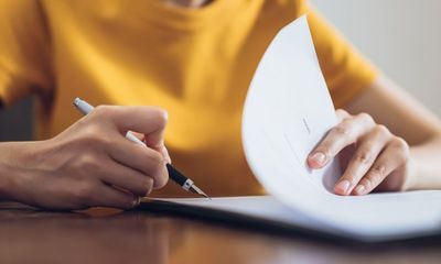 en voksen person med gul genser som signerer et dokument. Vilkår for permitteringer