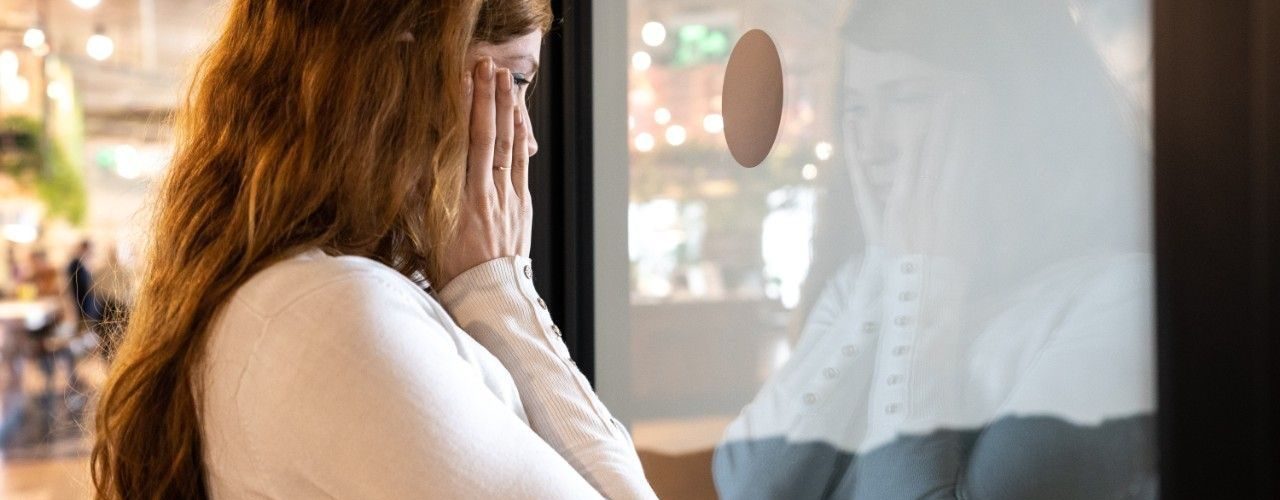 En kvinne holder seg på kinnene og ser ut gjennom en glassdør. Illustrasjon til sak om vilkår for permittering