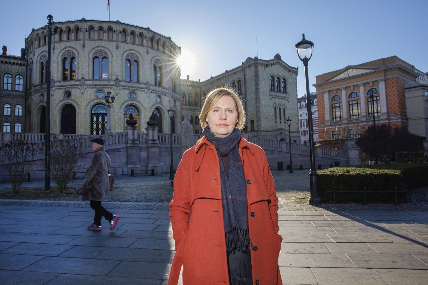 Mari Teigen, likestillingsforsker, utenfor stortinget i Oslo. En mann passerer henne i bakgrunn. 