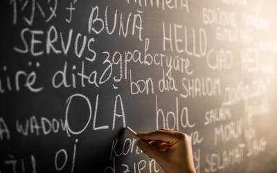 Illustrasjonsfoto av en tavle med ordet "hei" skrevet på flere ulike språk. Foto: Istock.