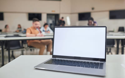 En laptop med blank skjerm står på et bord i et klasserom. Bilde.