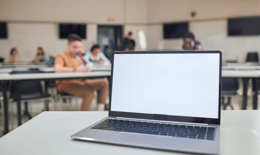 En laptop med blank skjerm står på et bord i et klasserom. Bilde.
