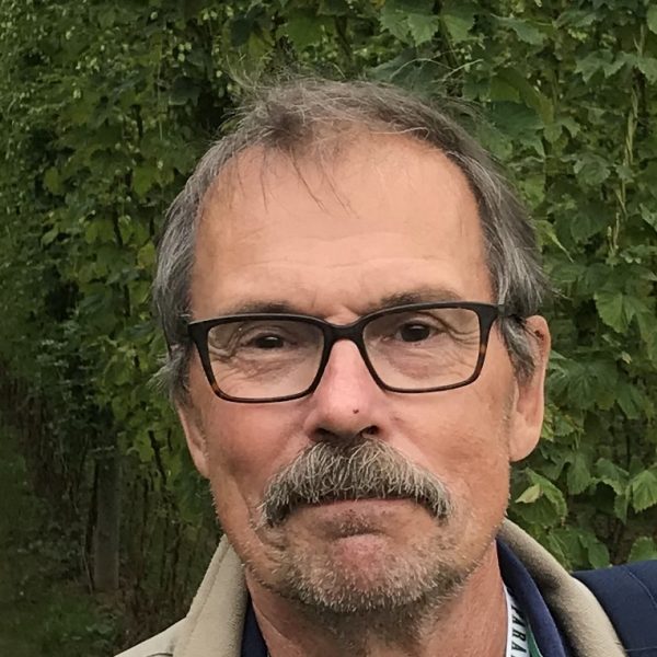En man med glasögon och mustasch framför en grön bakgrund