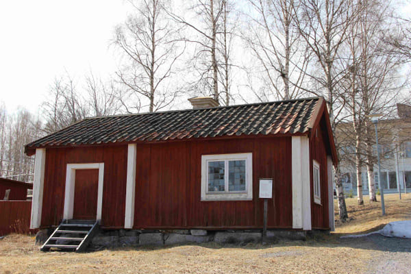 en röd timrad stuga med tegeltak och ett fönster med många spröjs